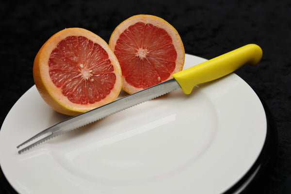 Full length view of knife in front of grapefruit sliced in half.